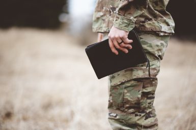 A shallow focus shot of a young soldier holding a book in a field