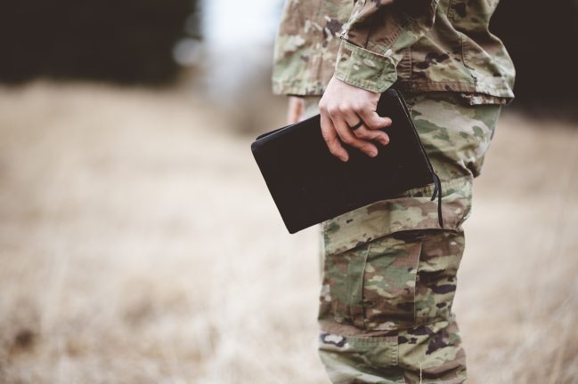 A shallow focus shot of a young soldier holding a book in a field