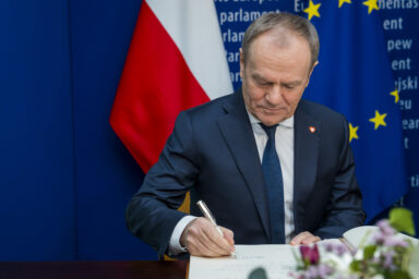 Donald Tusk writing on a desk, pictured with EU flag