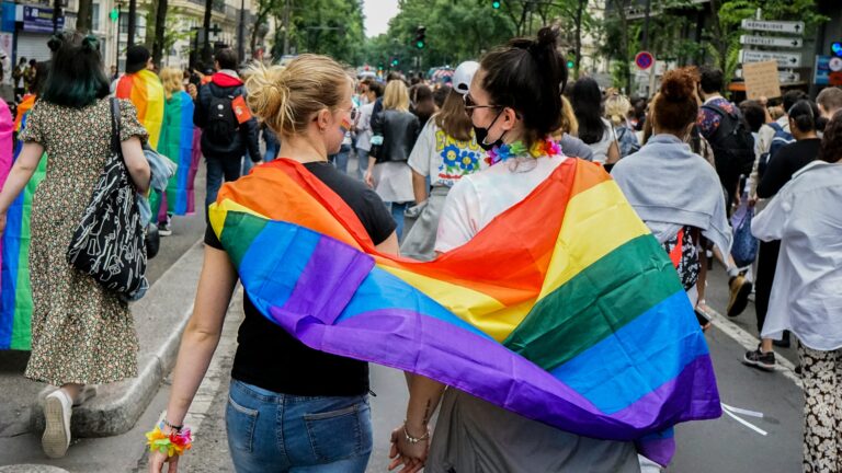 Young women draped in rainbow flag walking in a gay pride parade