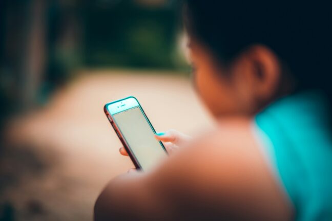 A silhouette of a child looking intently at a glowing smartphone screen