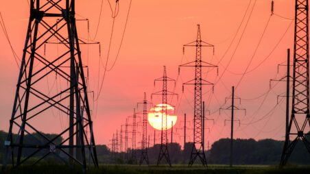 High-voltage power lines at sunset, silhouetted against an orange sky