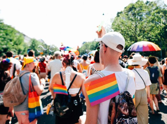 Pride march participants carrying rainbow flags in a sunny street