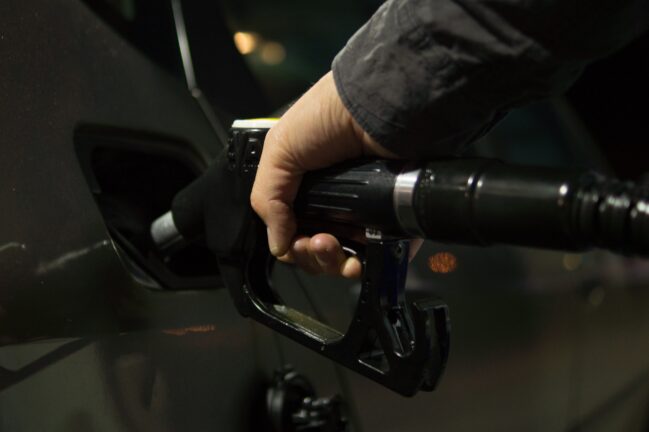 Close-up of a hand inserting a fuel nozzle into a vehicle’s gas tank