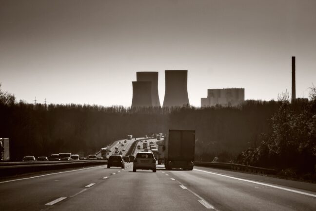 Cars and a truck on a motorway with power plant cooling towers in the background