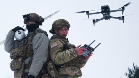 Two Ukrainian drone operators with a drone hovering in the background