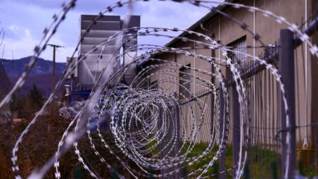 Close-up of barbed wire fence, with a prison building in the background