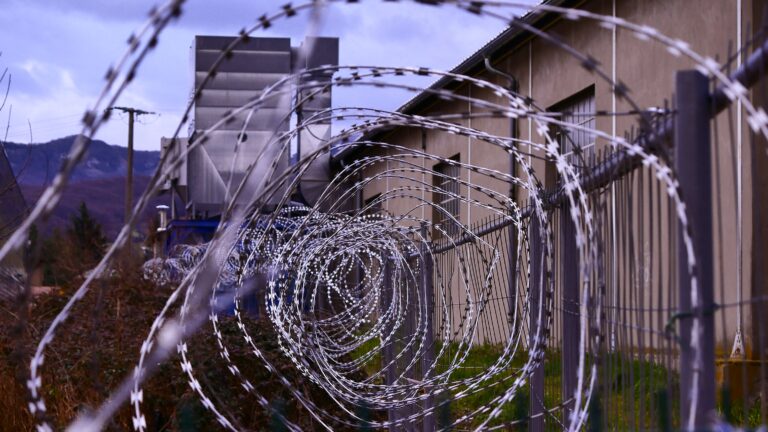 Close-up of barbed wire fence, with a prison building in the background
