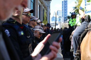 Police officers in a crowd, several looking at mobile phones