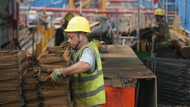 A Chinese factory worker stacking metal rods in a production facility