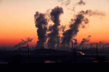 Industrial facility emitting smoke against a red sunset sky