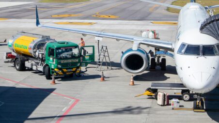 Fuel tanker refueling an aircraft through a wing-mounted fueling point on the airport tarmac.