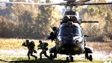 Armed NATO soldiers jump from a military helicopter during a live training exercise
