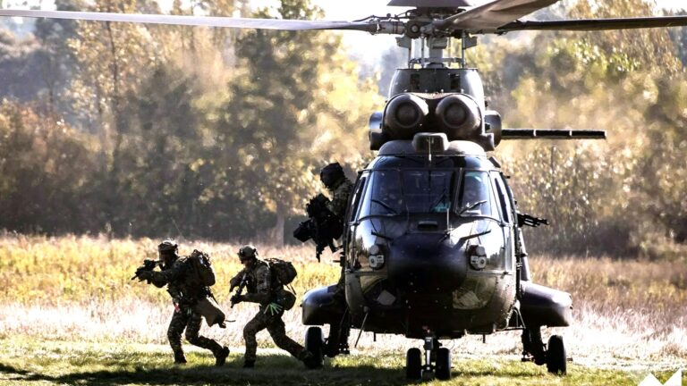 Armed NATO soldiers jump from a military helicopter during a live training exercise
