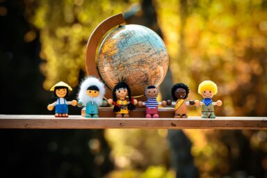 Wooden dolls representing cultures of the world standing hand in hand in front of a globe