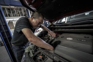 A mechanic working under the bonnet of a car in a garage