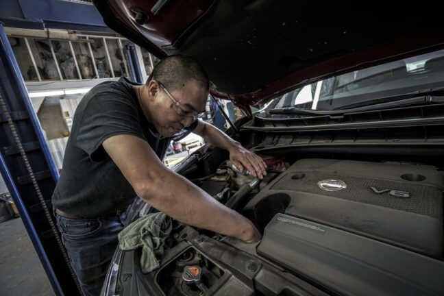 A mechanic working under the bonnet of a car in a garage