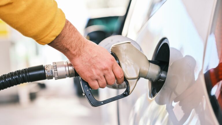A hand holding a fuel nozzle inserted into a car’s fuel tank during refuelling at a petrol station