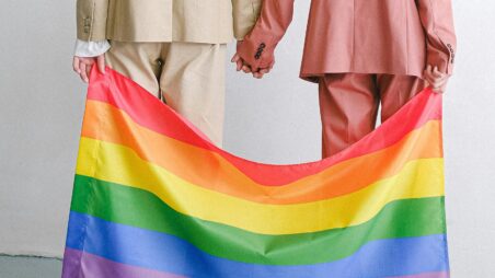 A same-sex couple holding hands over a rainbow LGBTIQ+ flag
