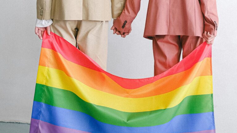 A same-sex couple holding hands over a rainbow LGBTIQ+ flag