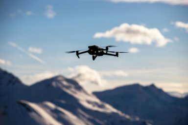 A drone flies against a backdrop of snowy mountains