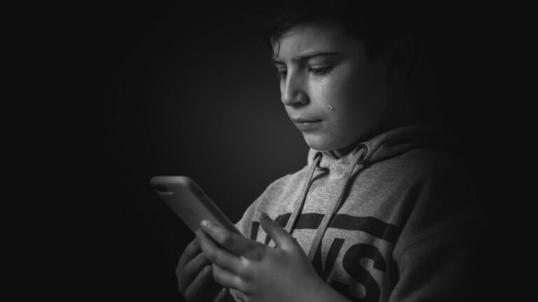 A boy looking at a smartphone screen, tearing up
