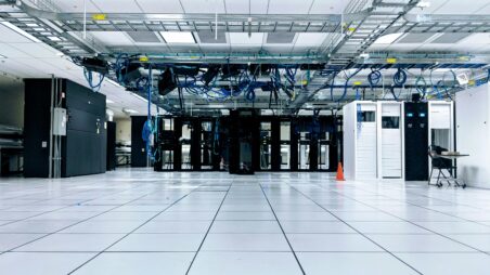A data centre with black server racks, blue cables overhead, and a white tiled floor