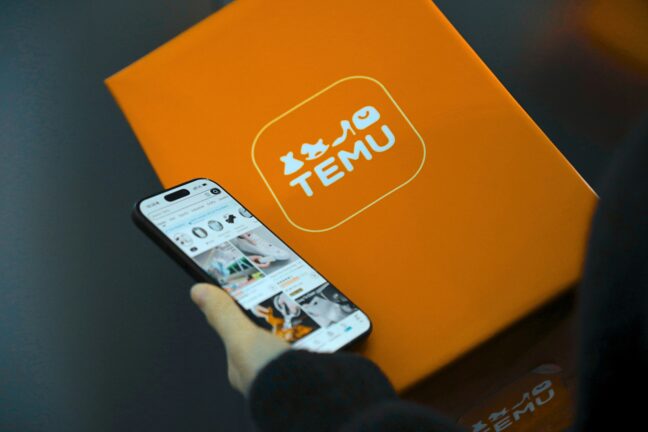 A person holding a smartphone next to a parcel box with the Temu logo