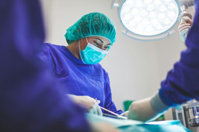 A healthcare professional wearing surgical scrubs, mask and gloves during a medical procedure