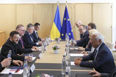 Volodymyr Zelensky in a bilateral meeting with European Council leaders at a table with EU and Ukrainian flags in the background