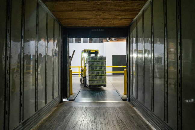 A forklift unloads cargo at a warehouse loading dock at night.