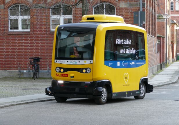 A small yellow autonomous minibus driving on a street in Germany.