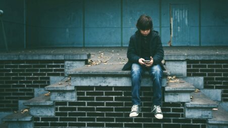 A boy sitting on steps and looking at a smartphone screen