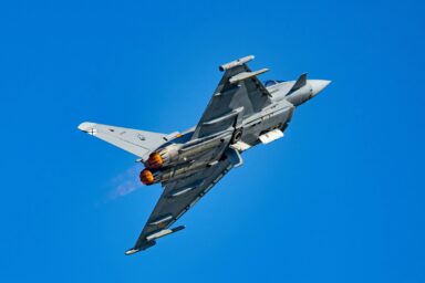 A Eurofighter Typhoon fighter jet climbing with afterburners lit against a blue sky