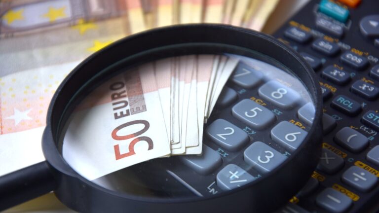 A magnifying glass resting on €50 banknotes and a calculator
