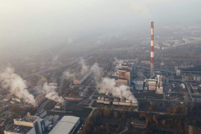 Aerial view of an industrial facility with smokestacks and steam, surrounded by fog