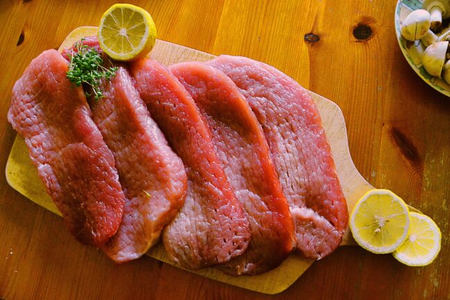Raw meat slices on a wooden board with lemon slices