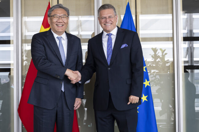 Maroš Šefčovič and Wang Wentao shaking hands in front of EU and Chinese flags at the European Commission in Brussels