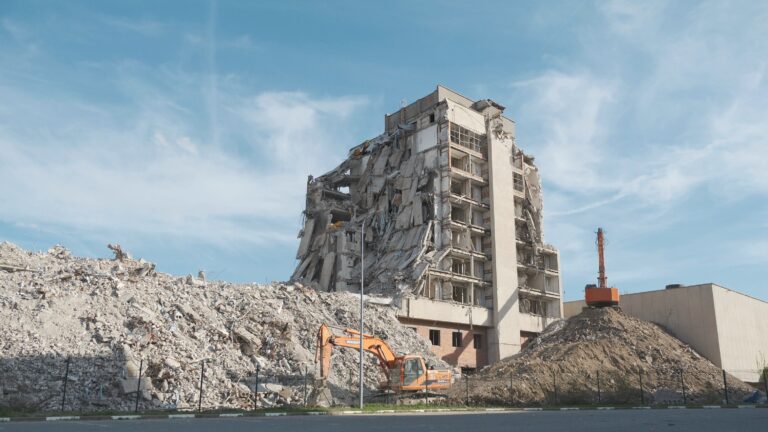 A partially demolished multi-storey building with rubble and excavators on site.