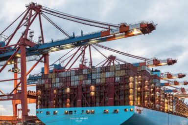A Maersk container ship being loaded at a port terminal with large cargo cranes