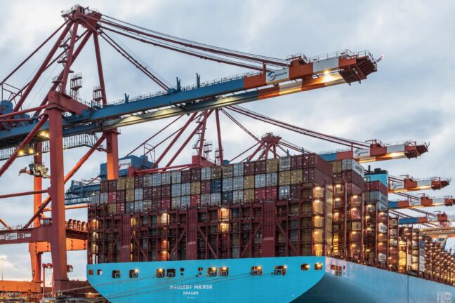 A Maersk container ship being loaded at a port terminal with large cargo cranes