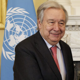 António Guterres smiling in front of a UN flag