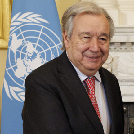 António Guterres smiling in front of a UN flag
