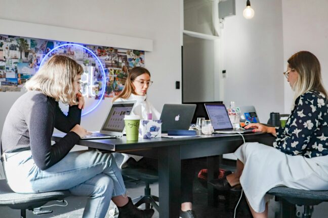Three women working on laptops in a modern office space