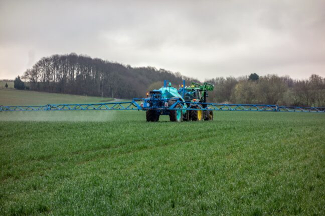Tractor spraying a green field under an overcast sky