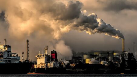 Industrial complex with a large smokestack emitting smoke behind a cargo port