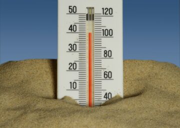 A thermometer stuck in sand shows a high temperature reading.