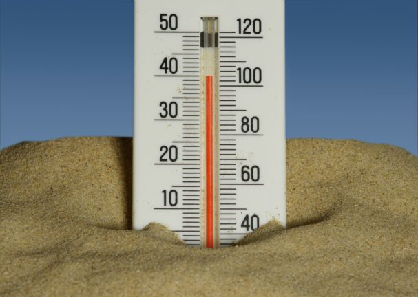 A thermometer stuck in sand shows a high temperature reading.