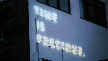 A building wall with a neon sign reading “Time is precious.”