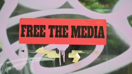 A wall covered with graffiti and a sticker reading "Free the media"